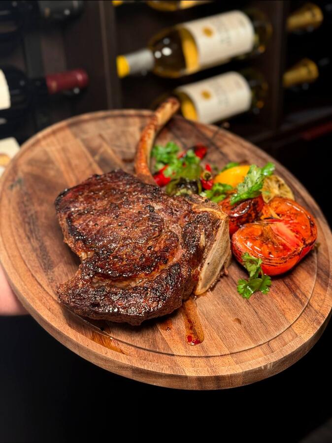 Bone-in ribeye on a wooden board with charred tomato